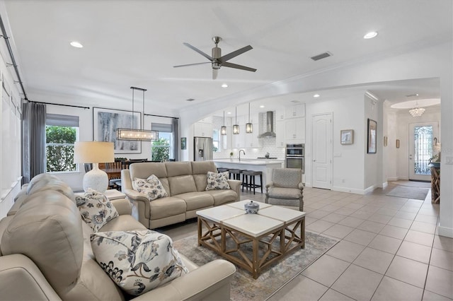 tiled living room featuring ceiling fan with notable chandelier, sink, and crown molding