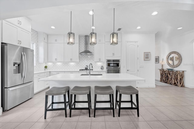 kitchen with wall chimney range hood, decorative backsplash, a kitchen island with sink, light tile patterned floors, and stainless steel appliances