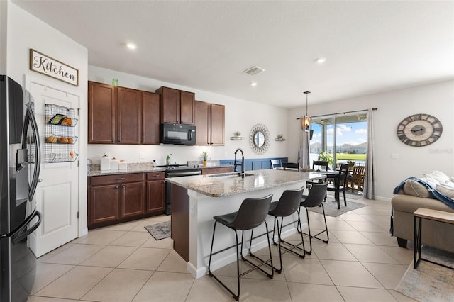 kitchen with a kitchen island with sink, a kitchen breakfast bar, light stone counters, sink, and appliances with stainless steel finishes