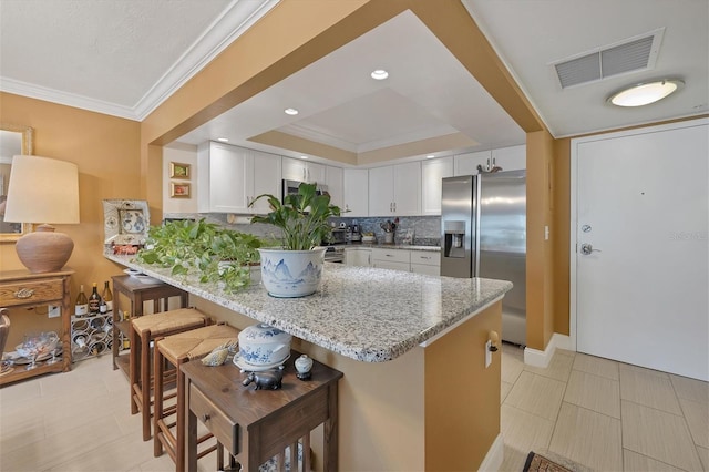 kitchen featuring visible vents, white cabinets, stainless steel fridge, a peninsula, and a kitchen breakfast bar