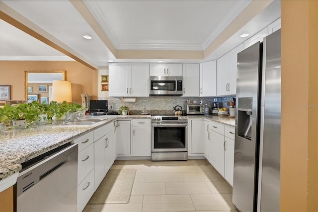 kitchen with white cabinets, appliances with stainless steel finishes, ornamental molding, a sink, and backsplash