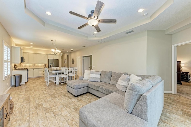 living room featuring light wood-type flooring, ceiling fan with notable chandelier, and a raised ceiling