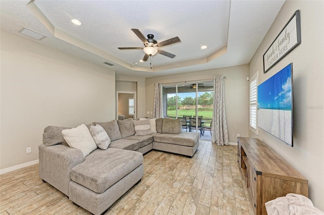 living room featuring light wood-type flooring, a textured ceiling, a tray ceiling, and ceiling fan