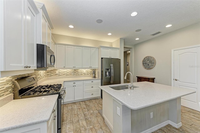 kitchen featuring appliances with stainless steel finishes, light hardwood / wood-style floors, a kitchen island with sink, sink, and white cabinetry