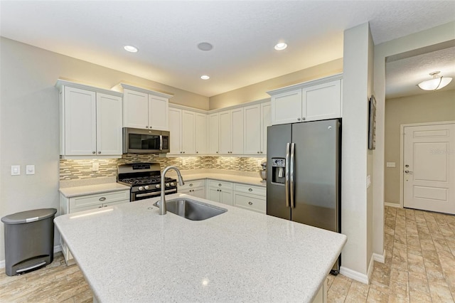 kitchen featuring white cabinets, appliances with stainless steel finishes, a center island with sink, and sink