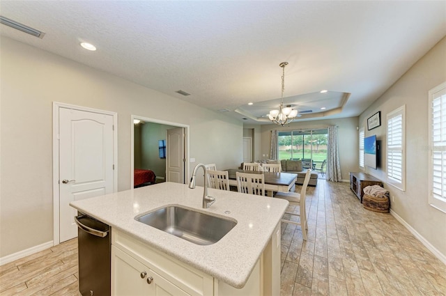 kitchen featuring light wood-type flooring, a notable chandelier, sink, hanging light fixtures, and a center island with sink