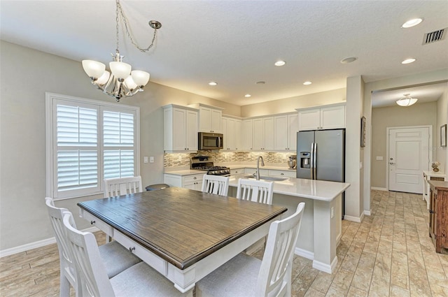 dining room with a textured ceiling, a chandelier, sink, and light hardwood / wood-style floors