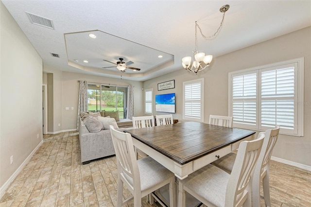 dining area featuring ceiling fan with notable chandelier, a raised ceiling, and light hardwood / wood-style flooring