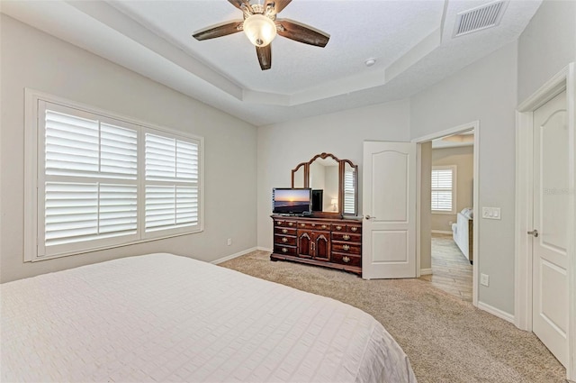 bedroom featuring ceiling fan, light colored carpet, and a raised ceiling