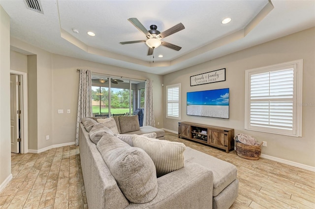 living room featuring a tray ceiling, ceiling fan, and light hardwood / wood-style floors