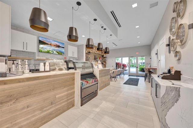 kitchen with light stone counters, tasteful backsplash, white cabinets, decorative light fixtures, and french doors