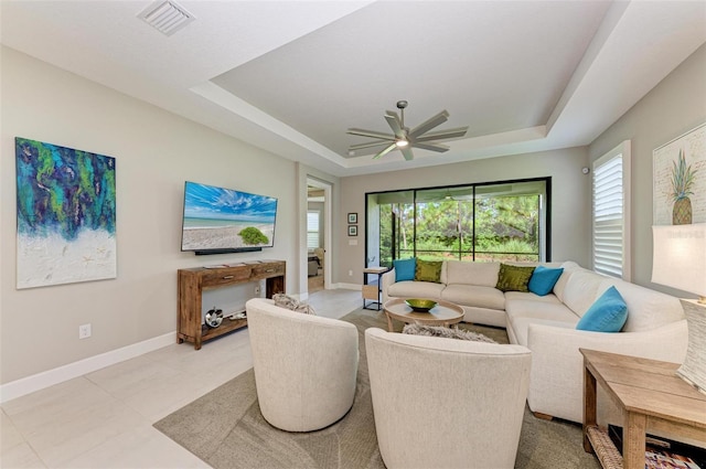 tiled living room with a healthy amount of sunlight, ceiling fan, and a tray ceiling