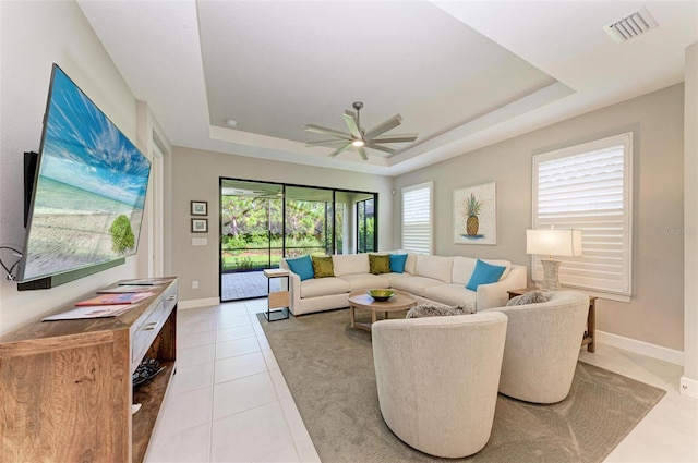 living room featuring light tile patterned floors, ceiling fan, and a tray ceiling