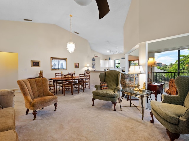 carpeted living room with ceiling fan with notable chandelier and high vaulted ceiling