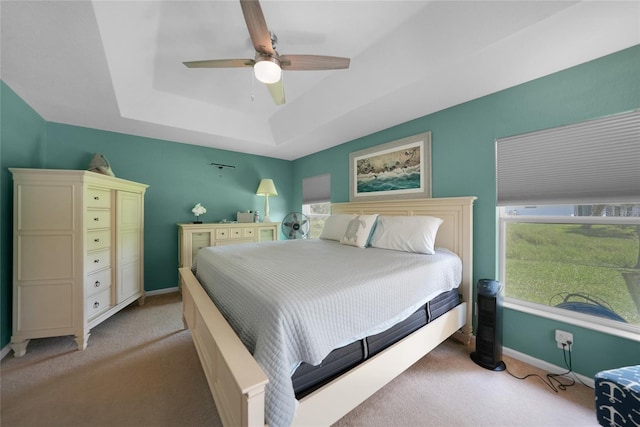 bedroom featuring ceiling fan, light colored carpet, multiple windows, and a tray ceiling