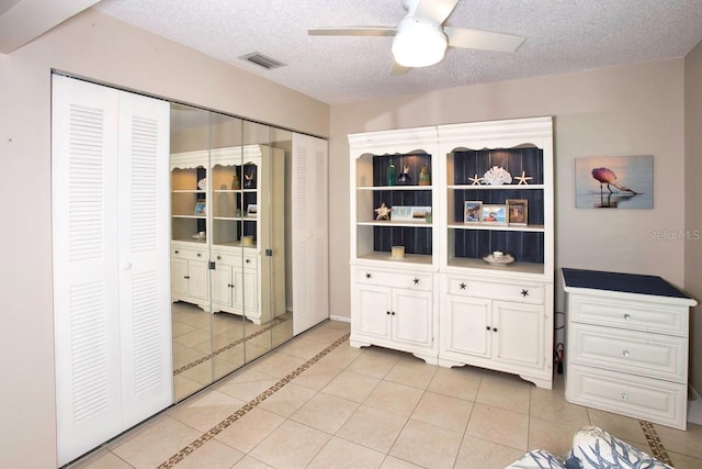 interior space with a textured ceiling, ceiling fan, and light tile patterned floors