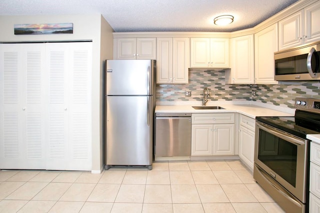 kitchen with sink, appliances with stainless steel finishes, decorative backsplash, light tile patterned floors, and cream cabinetry