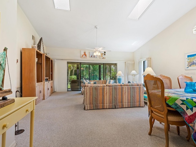 interior space with ceiling fan, light colored carpet, and vaulted ceiling with skylight