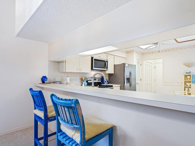 kitchen with a textured ceiling, backsplash, appliances with stainless steel finishes, carpet floors, and white cabinets