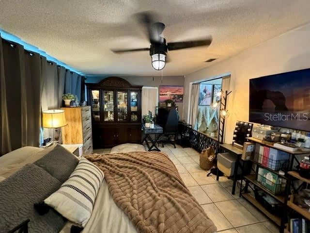 bedroom with light tile patterned floors, visible vents, a ceiling fan, and a textured ceiling