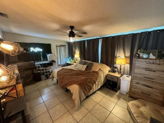 bedroom featuring a ceiling fan, visible vents, a textured ceiling, and light tile patterned floors