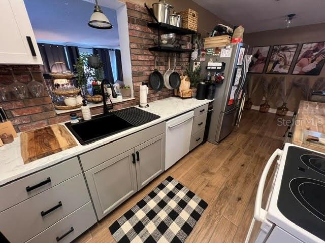 kitchen featuring white appliances, pendant lighting, light hardwood / wood-style floors, sink, and white cabinets