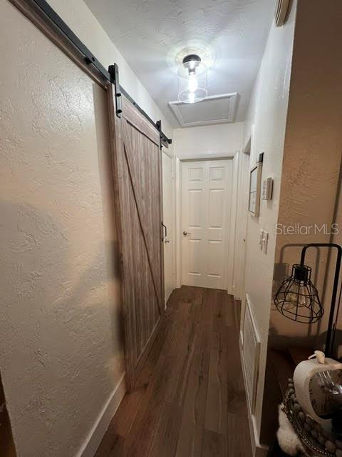 hall featuring dark wood-style flooring, a textured wall, and a barn door