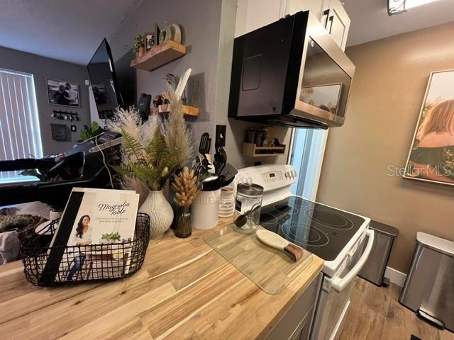 kitchen with white range with electric cooktop, stainless steel microwave, white cabinetry, wood finished floors, and baseboards