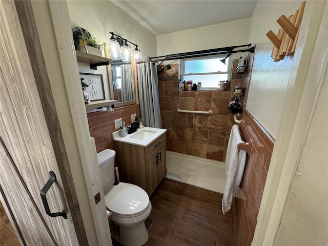 bathroom with a stall shower, toilet, wood finished floors, vanity, and tile walls