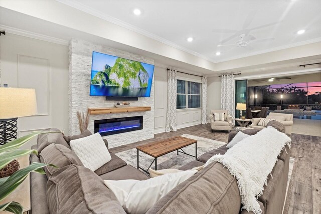 living room featuring ceiling fan, a stone fireplace, crown molding, and light hardwood / wood-style flooring