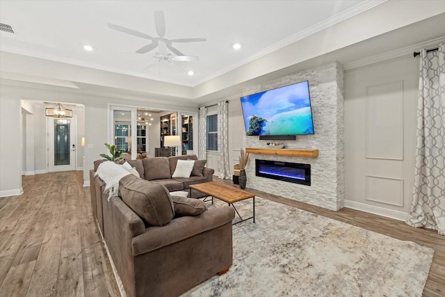 living room featuring ceiling fan with notable chandelier, hardwood / wood-style flooring, a stone fireplace, and crown molding