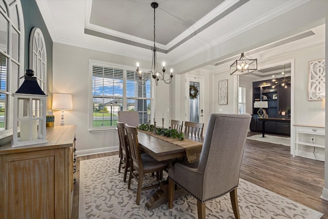 dining area with a chandelier, hardwood / wood-style floors, a raised ceiling, and crown molding