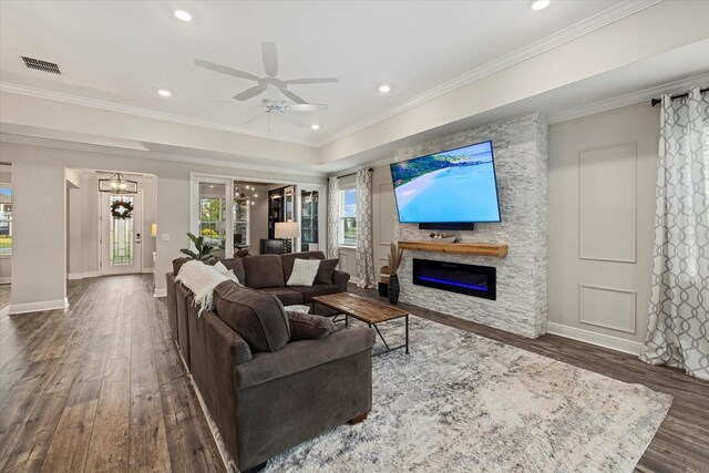 living room with ceiling fan with notable chandelier, a stone fireplace, ornamental molding, and dark wood-type flooring