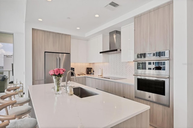 kitchen featuring a center island with sink, wall chimney range hood, sink, tasteful backsplash, and stainless steel appliances