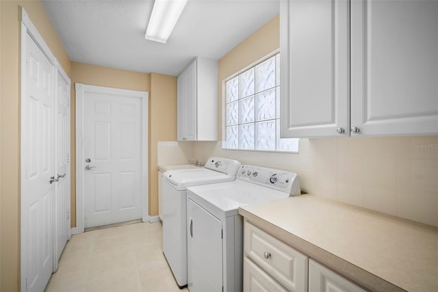 clothes washing area with washing machine and dryer, cabinets, and light tile patterned floors