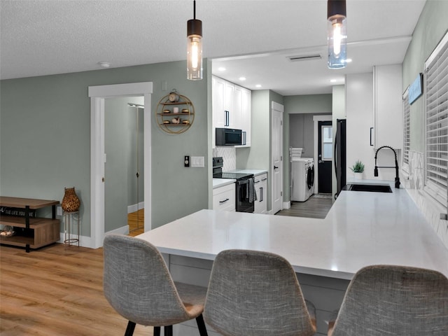 kitchen with sink, light wood-type flooring, washing machine and clothes dryer, white cabinetry, and black appliances