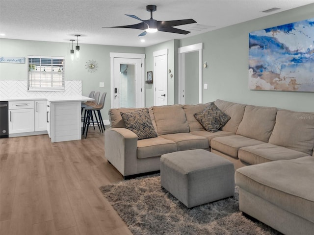 living room with a textured ceiling, ceiling fan, and light wood-type flooring