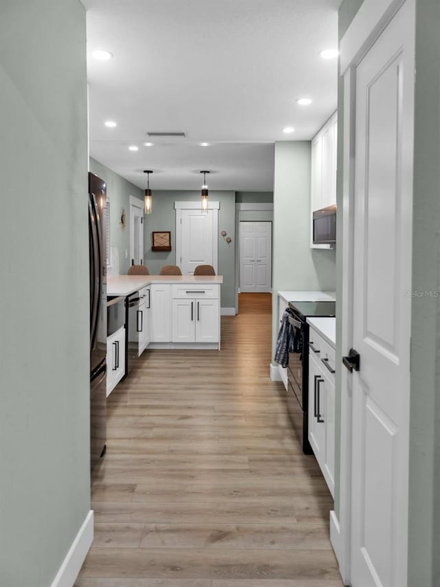 kitchen with hanging light fixtures, light wood-type flooring, appliances with stainless steel finishes, white cabinetry, and kitchen peninsula