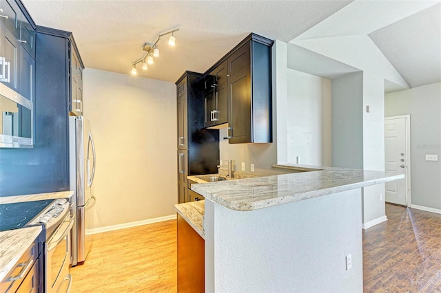 kitchen with a sink, a peninsula, appliances with stainless steel finishes, and wood finished floors