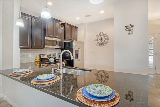 kitchen with backsplash, stainless steel appliances, dark brown cabinets, dark stone counters, and hanging light fixtures