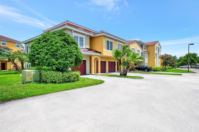 townhome / multi-family property featuring a front yard, a residential view, an attached garage, and stucco siding