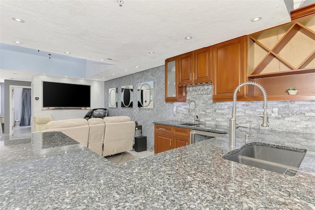 kitchen featuring glass insert cabinets, brown cabinets, a sink, and dark stone counters