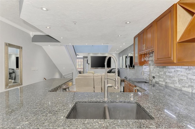 kitchen featuring decorative backsplash, dark stone counters, brown cabinets, a textured ceiling, and a sink