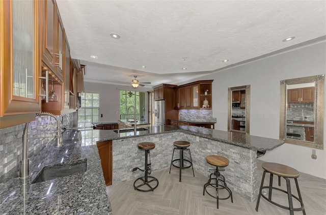 kitchen with a breakfast bar area, a peninsula, stainless steel appliances, a sink, and dark stone countertops