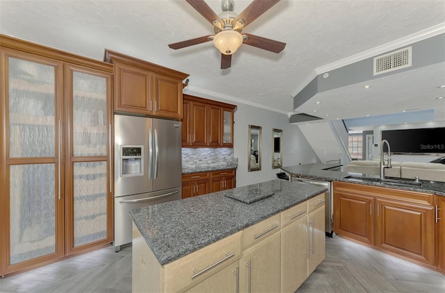 kitchen with visible vents, appliances with stainless steel finishes, glass insert cabinets, a kitchen island, and a sink