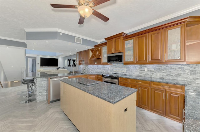 kitchen featuring a kitchen island, visible vents, appliances with stainless steel finishes, dark stone counters, and glass insert cabinets