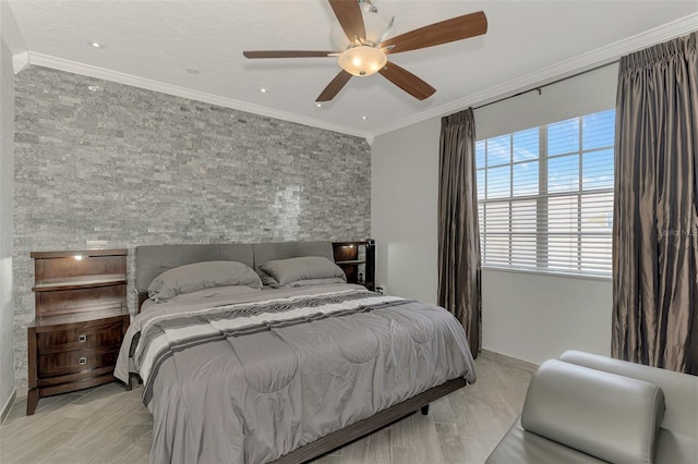 bedroom featuring ceiling fan, an accent wall, baseboards, light wood-type flooring, and crown molding