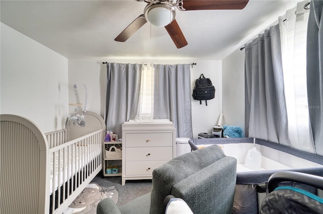 bedroom featuring ceiling fan, a nursery area, and carpet flooring