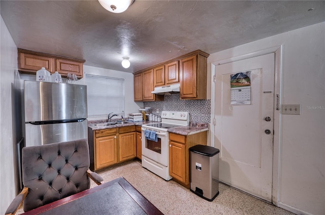 kitchen featuring white electric range oven, backsplash, stainless steel refrigerator, light stone countertops, and sink