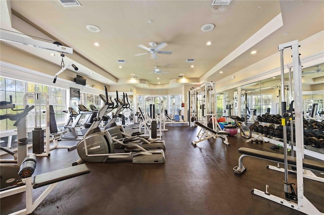 exercise room featuring a ceiling fan, a raised ceiling, visible vents, and plenty of natural light